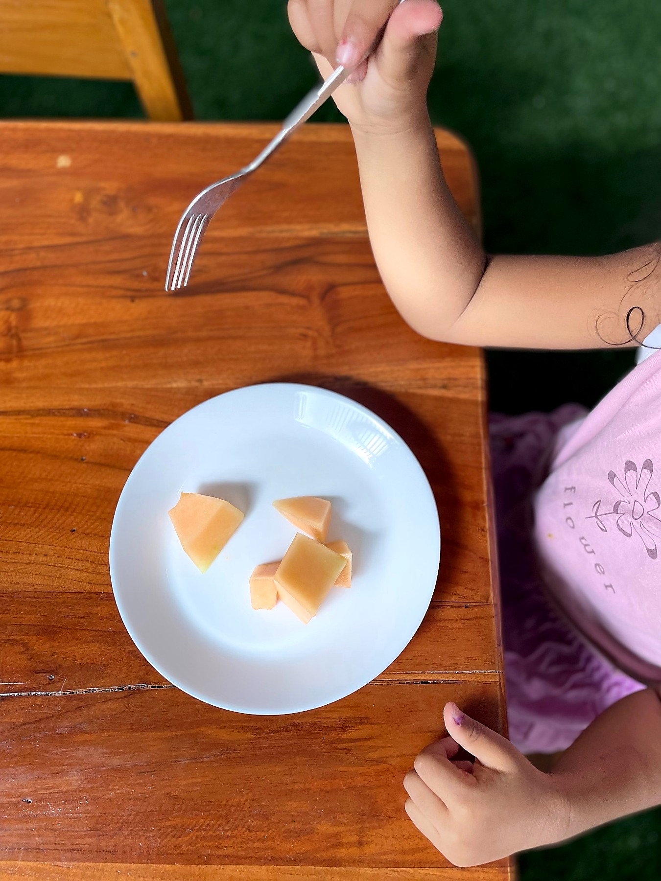A small hand reaching for cubes of fresh melon on a plate