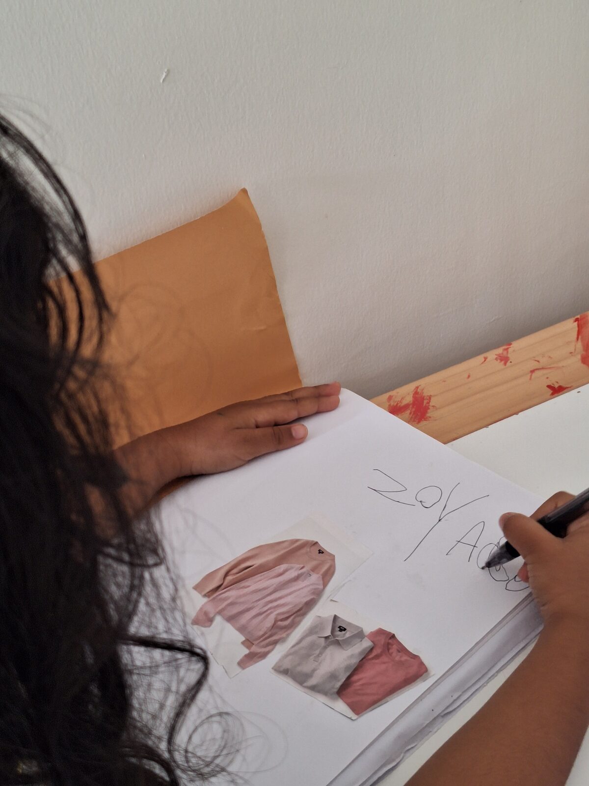 A child writing in a journal beside a collage of cut-out pictures during a guided session