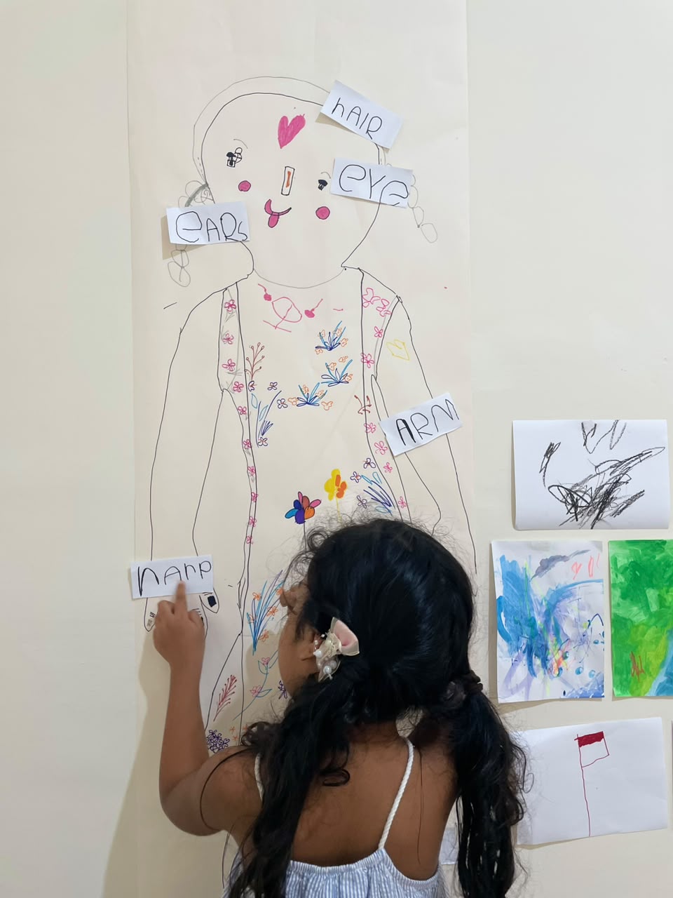 A child matching handwritten word cards to a large body drawing